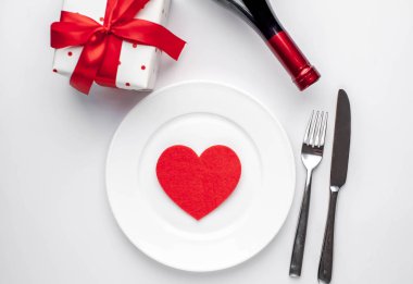 Table setting for Valentine's Day - white plate, wine, gift, kitchen appliances, hearts on a white background