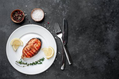 Beyaz tabakta ızgara somon bifteği ve arka planda baharatlar.