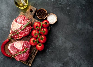 two raw beef steaks with tomatoes and spices on a concrete background 