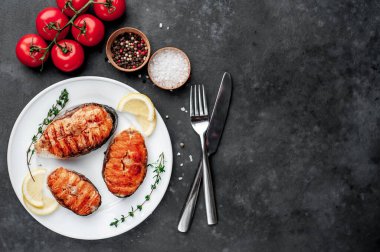 Three grilled salmon steaks in a white plate with spices on a stone background