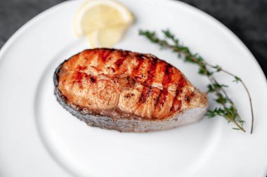 Grilled salmon steak in a white plate with spices on a stone background
