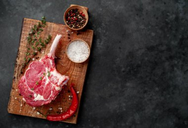raw beef steak, beef tomahawk with spices, thyme on a stone background.