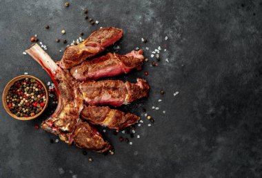 Sliced, grilled beef tomahawk with spices on a stone background with space for text 