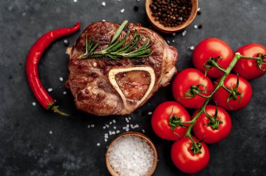 grilled steak, with tomatoes and spices on a stone background.