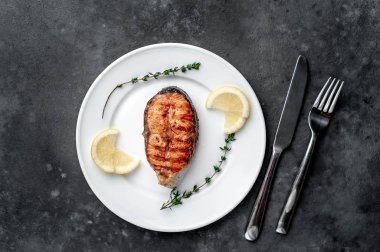 Grilled salmon steak in a white plate with spices on a stone background
