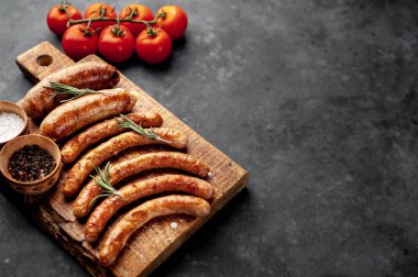 Çeşitli ızgara sosislerin yakın plan görüntüsü ve taş bir masada baharatlar.