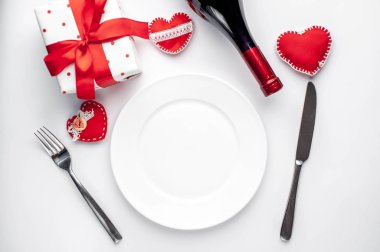 Table setting for Valentine's Day - white plate, wine, gift, kitchen appliances, hearts on a white background