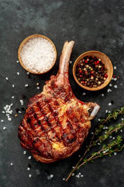 steak - grilled beef tomahawk with spices, thyme on a stone background