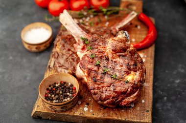grilled beef steaks - tomahawk with tomatoes and red pepper on a stone background