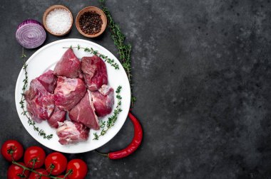 fresh sliced ??raw beef meat in a white bowl on a stone background with tomatoes and spices