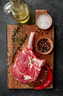 raw beef steak, beef tomahawk with spices, thyme on a stone background.