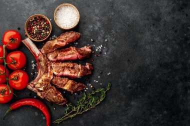 Sliced, grilled beef tomahawk with spices on a stone background with space for text 