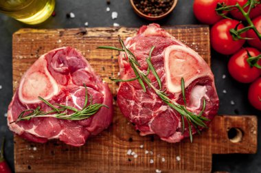 Beton zeminde domates ve baharatlı iki çiğ bifteğin yakın plan görüntüsü. 