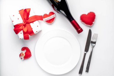 Table setting for Valentine's Day - white plate, wine, gift, kitchen appliances, hearts on a white background