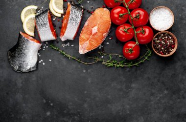 fresh raw salmon steaks and salmon tail on a stone background with salt, pepper, tomatoes, lemon with copy space for your text