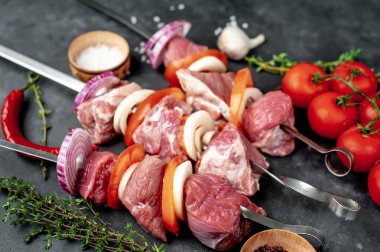 Çiğ et şişlerinin açılı görüntüsü. Arka planda sebzeli ve baharatlı ızgara et..