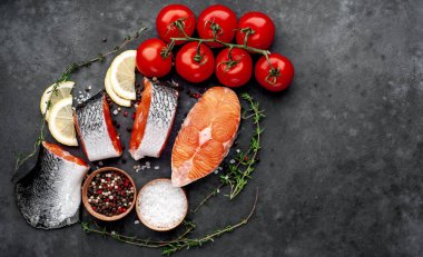 fresh raw salmon steaks and salmon tail on a stone background with salt, pepper, tomatoes, lemon with copy space for your text