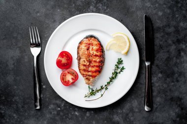 Grilled salmon steak in a white plate with spices on a stone background