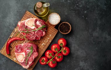 two raw beef steaks with tomatoes and spices on a concrete background 