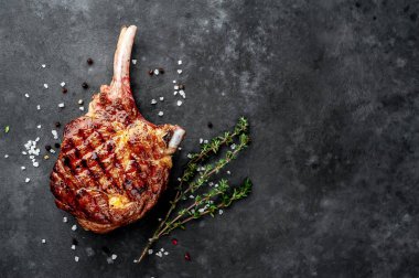 steak - grilled beef tomahawk with spices, thyme on a stone background