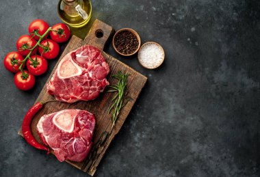 two raw beef steaks with tomatoes and spices on a concrete background 