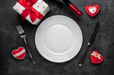 Table setting for Valentine's Day - white plate, wine, gift, kitchen appliances, hearts on a stone backgroundA