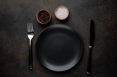 Taş bir arka planda çatal ve bıçaklı baharatlı siyah tabak
