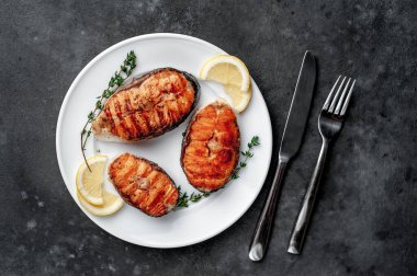 Three grilled salmon steaks in a white plate with spices on a stone background