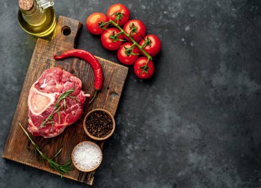 raw beef steak with tomatoes and spices on a stone background.