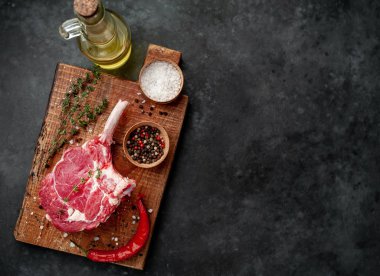 raw beef steak, beef tomahawk with spices, thyme on a stone background.