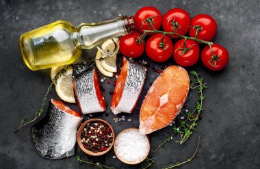 fresh raw salmon steaks and salmon tail on a stone background with salt, pepper, tomatoes, lemon with copy space for your text