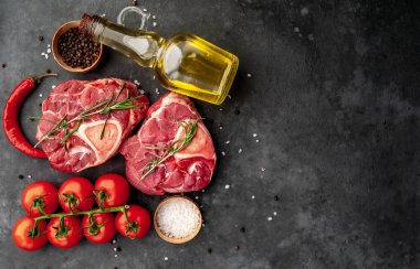 Beton arka planda domates ve baharatlı iki çiğ bifteğin üst görüntüsü. 