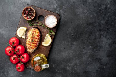 Grilled salmon steak with spices, lemon and tomatoes on a stone background.