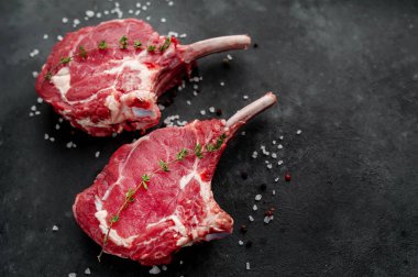 İki çiğ biftek, baharatlı dana baltası, arka planda kekik.