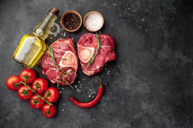 two raw beef steaks with tomatoes and spices on a concrete background 