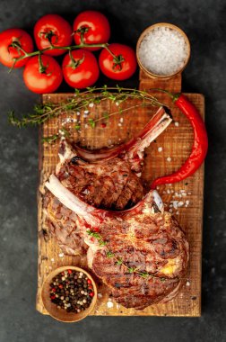 grilled beef steaks - tomahawk with tomatoes and red pepper on a stone background