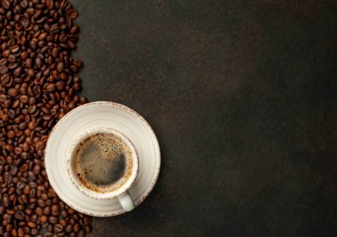 Top view of cup of tasty coffee and beans on a stone background with space for text 