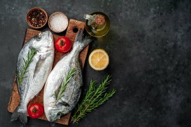 Baharatlı ve malzemeli taze dorado balığı domates, biberiye, ayçiçeği yağı, arkaplanda pişirmek için limon.