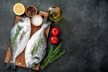 Baharatlı ve malzemeli taze dorado balığı domates, biberiye, ayçiçeği yağı, arkaplanda pişirmek için limon.