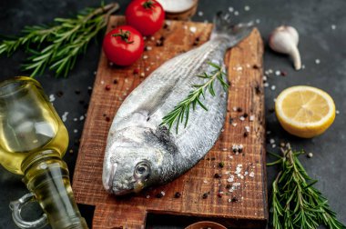 Baharatlı ve malzemeli taze dorado balığı domates, biberiye, ayçiçeği yağı, arkaplanda pişirmek için limon.