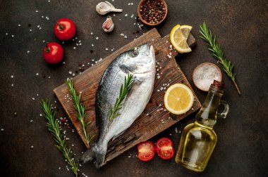 Baharatlı ve malzemeli taze dorado balığı domates, biberiye, ayçiçeği yağı, arkaplanda pişirmek için limon.