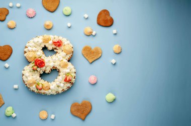 Çiçeklerle süslenmiş 8 numaralı pasta, krem peynir, marşmelov, mavi arka planda Bizet. Uluslararası Kadınlar Günü kartpostalı