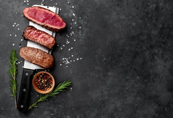 Three pieces of meat grilled over a meat knife Three types of frying meat, rare, medium, well done on stone background with copy space for your text