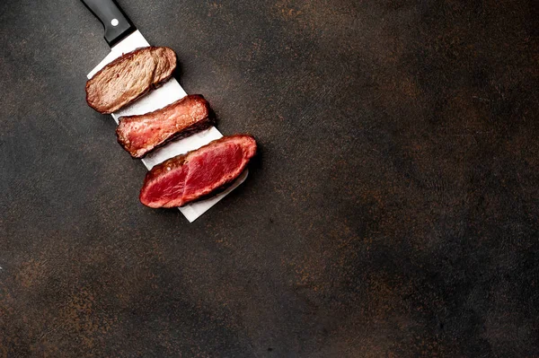 Three pieces of meat grilled over a meat knife Three types of frying meat, rare, medium, well done with spices on stone background with copy space for your text