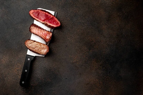 Three pieces of meat grilled over a meat knife Three types of frying meat, rare, medium, well done with spices on stone background with copy space for your text