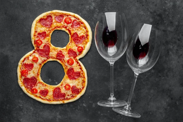 Pizza in form of 8, bottle of wine and glasses for International Women's Day on March 8 on a stone background