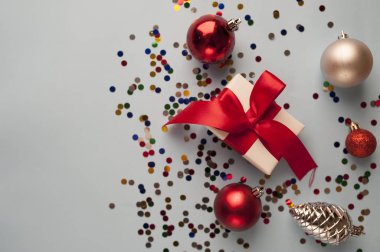 Beyaz arka planda beyaz hediye kutusuyla Noel kompozisyonu, kırmızı kurdeleli köknar dalları, oyuncaklar ve tebrik için kopya alanı