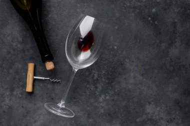 Kırmızı şarap şişesi, şarap kadehi ve tirbuşon taştan bir arka planda.