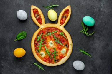 Yumurtalı tavşan şeklinde bayramlık Paskalya pizzası. Taş zeminde çok renkli Paskalya yumurtaları. Paskalya kutlaması kavramı.
