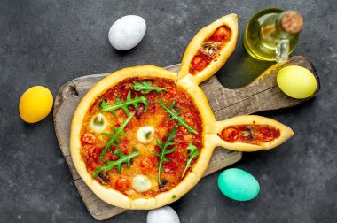 Yumurtalı tavşan şeklinde bayramlık Paskalya pizzası. Taş zeminde çok renkli Paskalya yumurtaları. Paskalya kutlaması kavramı.